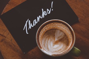 Mug Of Coffee On Wood Table With Black Card That Says "Thanks!"